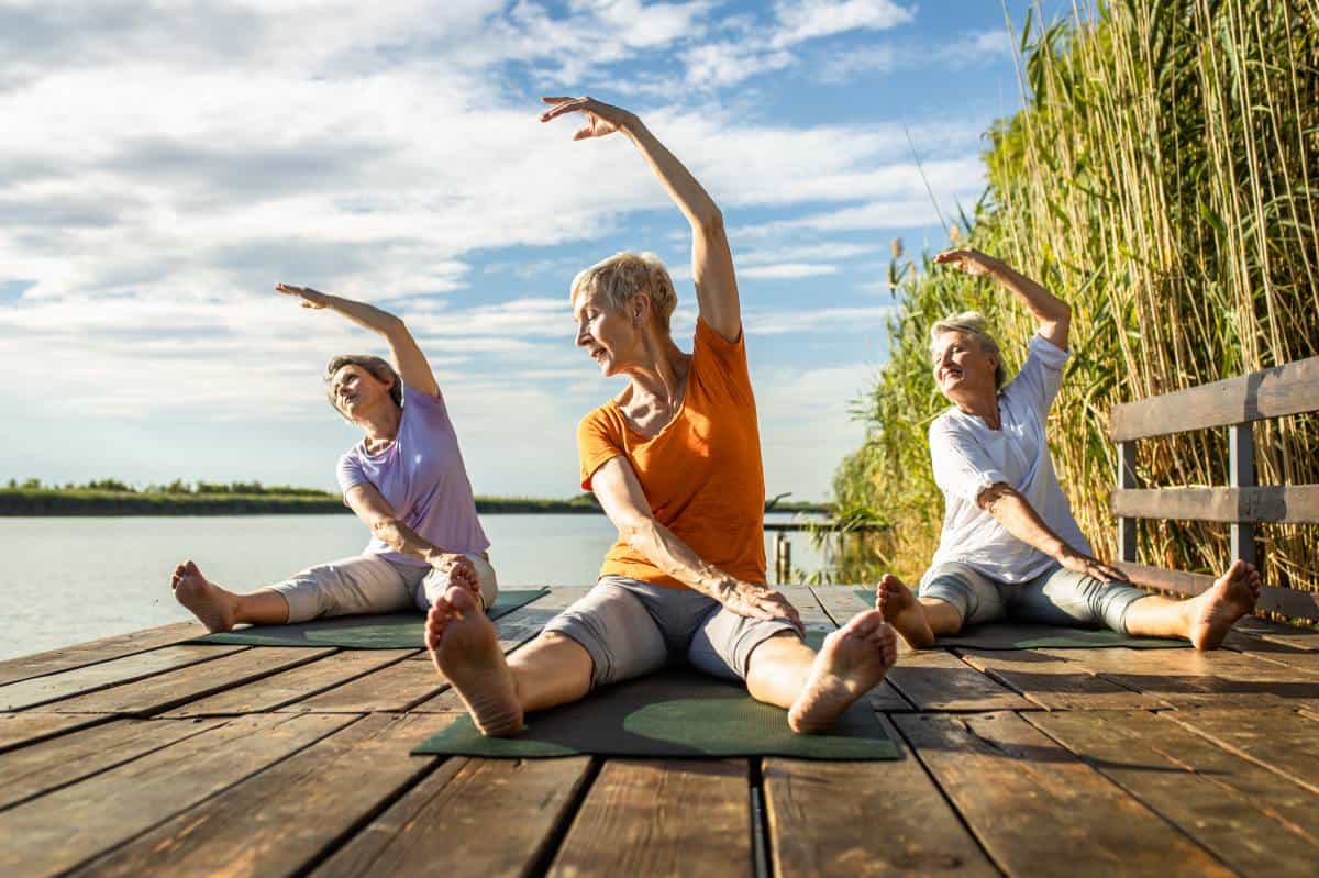 Group of senior woman doing yoga exercises by the lake.